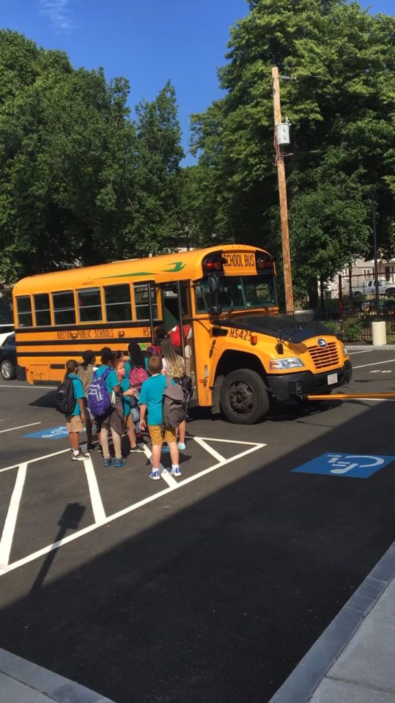 A video of children in teal shirts getting on the bus at the end of the day