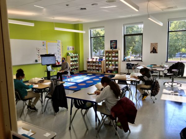 Students sit at desks in a classroom with lots of windows and a bright green wall