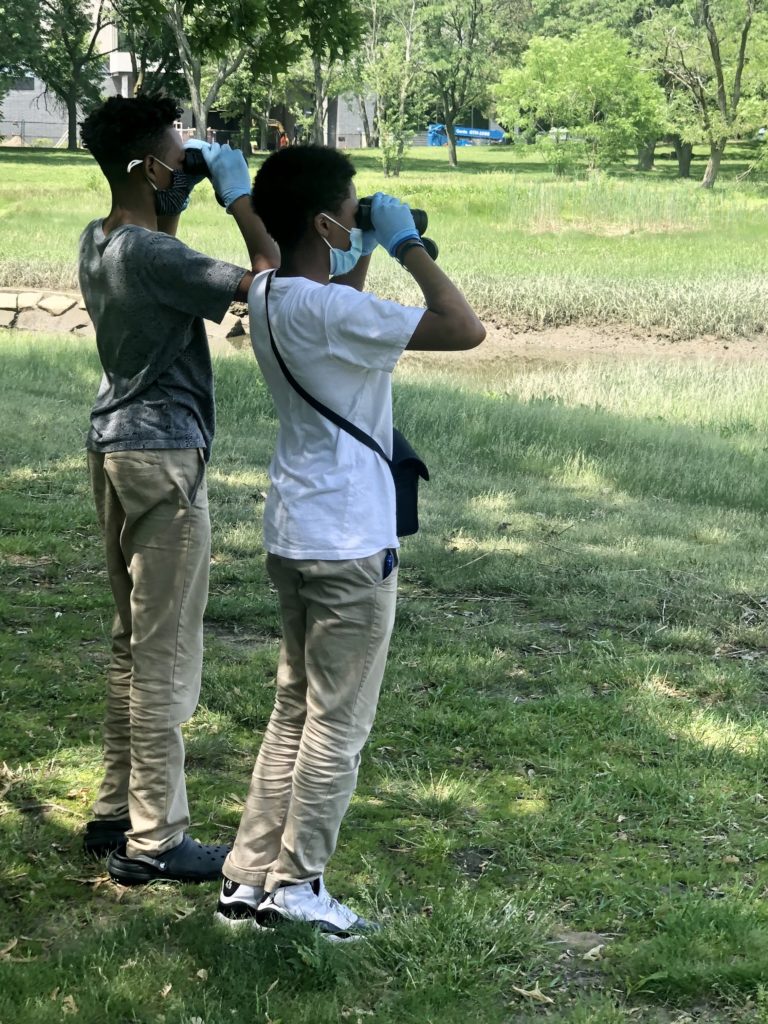 Two students who are black using binoculars to observe birds at Savin Hill Cove