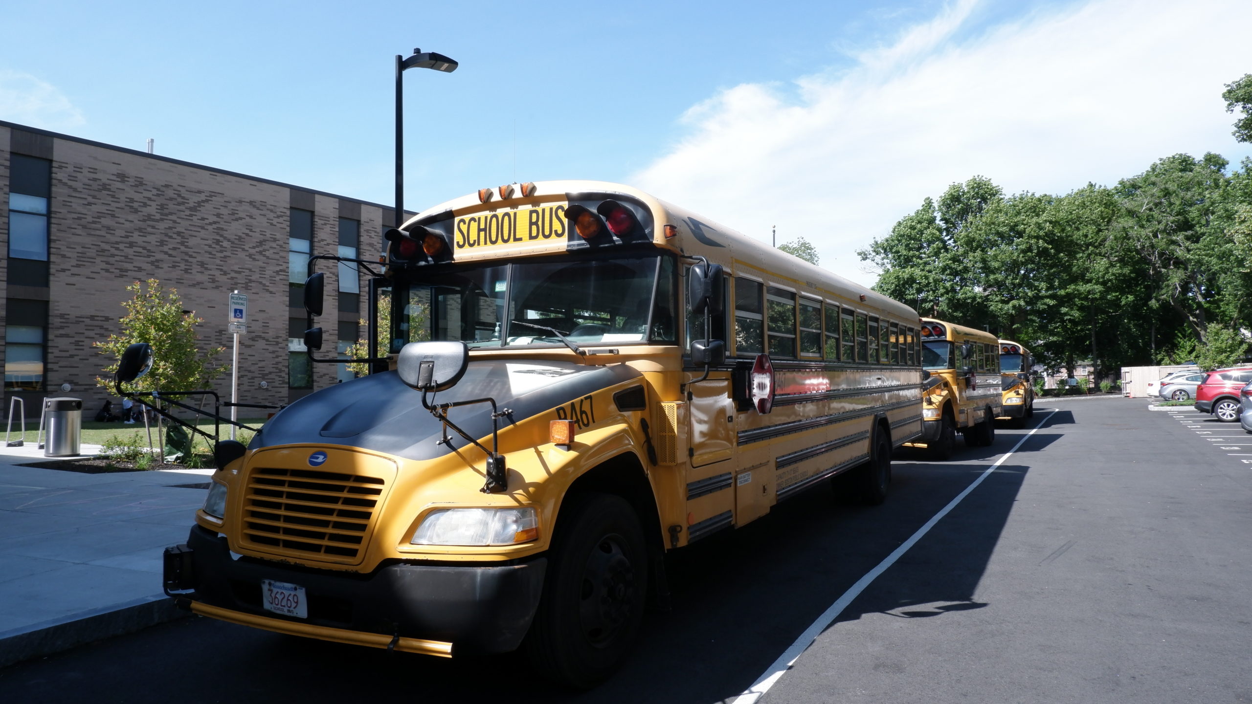A picture of a line of school buses in front of a light colored brick building (the Upper School).